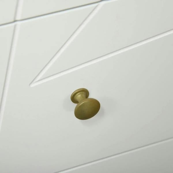 Close-up of white dresser drawer front with gold round knob and decorative panel seams.