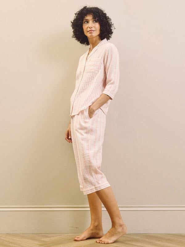 Woman wearing a light pink striped pyjama set against a plain background