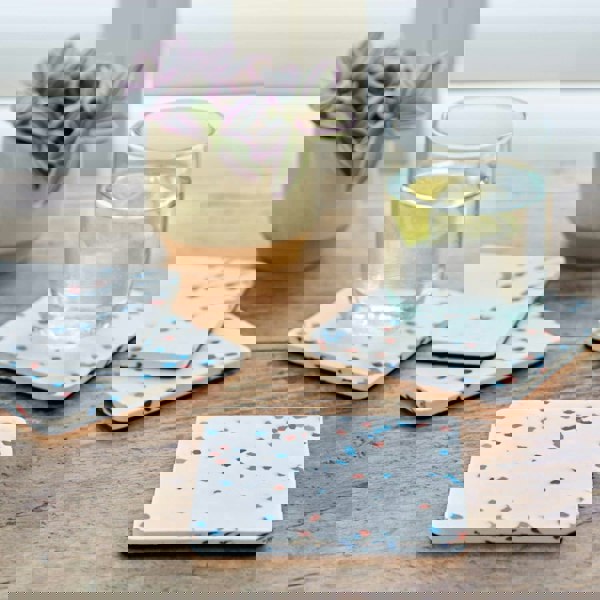 Four square plastic coasters made from recycled materials on a wooden table.