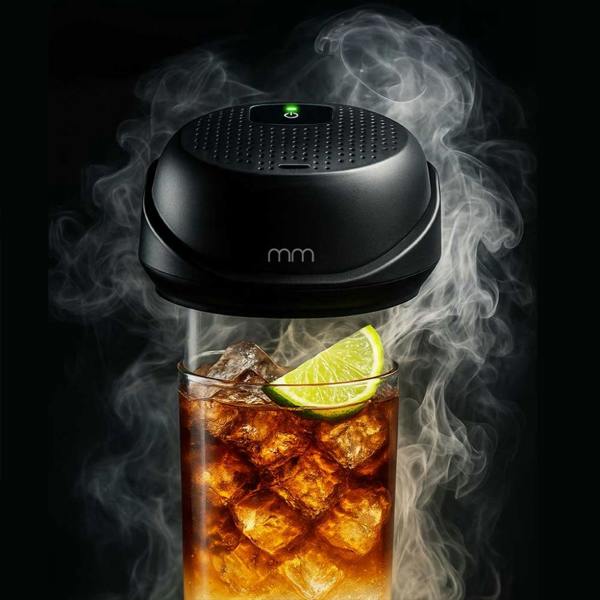 Close-up studio shot of a black electric cocktail smoker infusing a highball glass filled with an iced drink and a lime slice against a dark background with dense smoke.