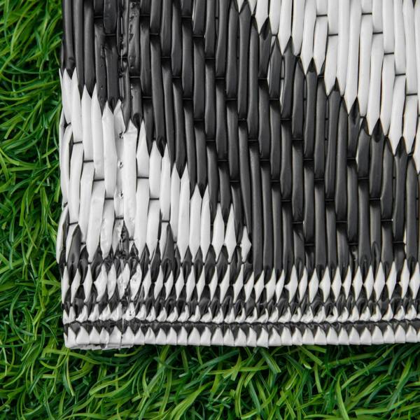 Corner of black-and-white outdoor rug with textured woven stripes and fringe-like edge.