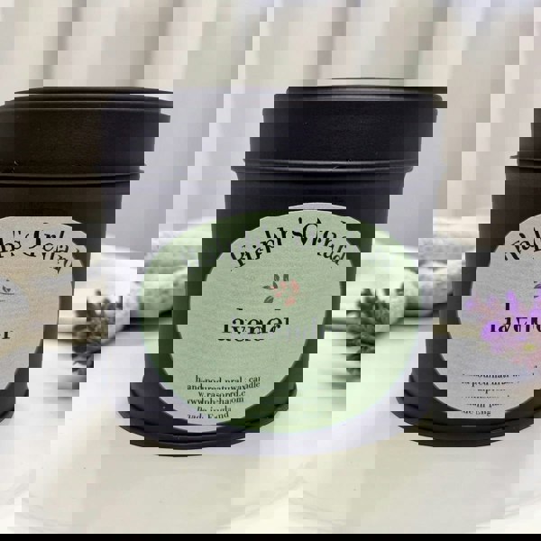 Candle tin labeled 'Ralph's Orchard lavender' on a white surface with a blurred background