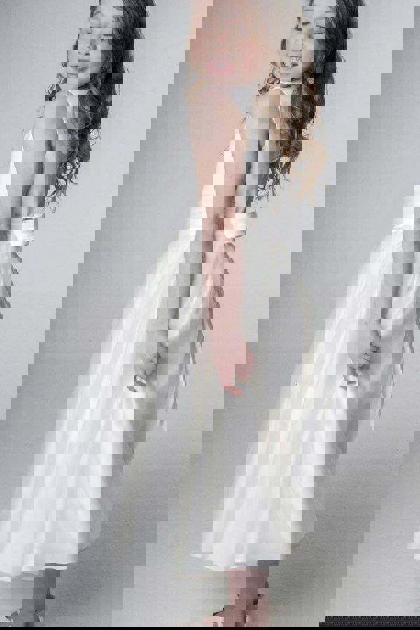 Young girl wearing a white dress with a belt on a plain background