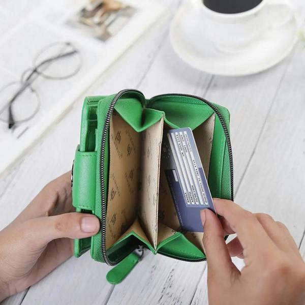 Green wallet with a card being inserted on a white surface with glasses and a cup.
