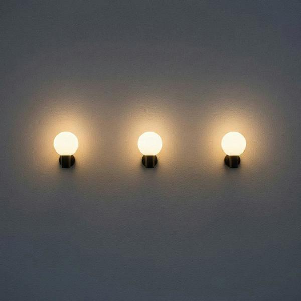 black globe outdoor wall light with 3 lights mounted in a row along a white wall outside