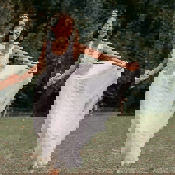 Young girl in a white dress standing outdoors with greenery in the background