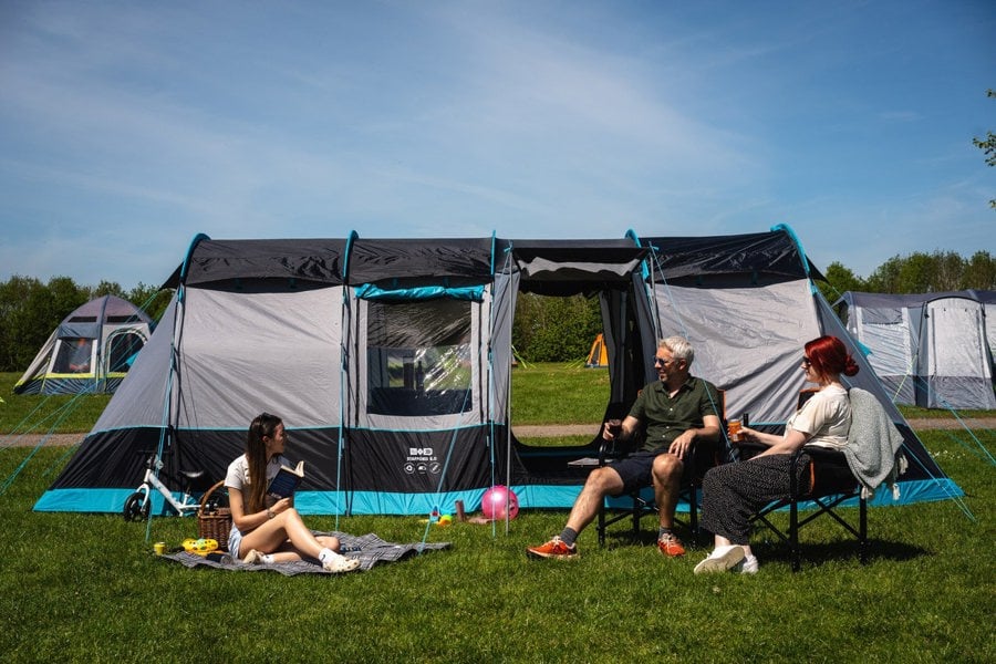 A couple and their daughter use camping furniture tp picnic outside the Stafford 8.0 poled family tent