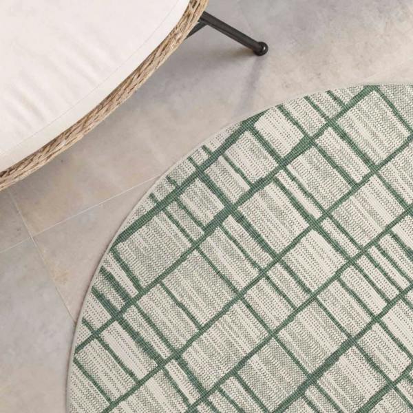 Round green and white checkered rug on a tiled floor with a wicker chair.