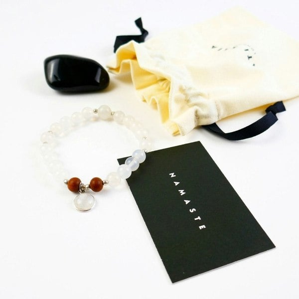 Kati Kaia Selene purity mala bracelet with white beads and brown accents beside a Namaste card and drawstring pouch