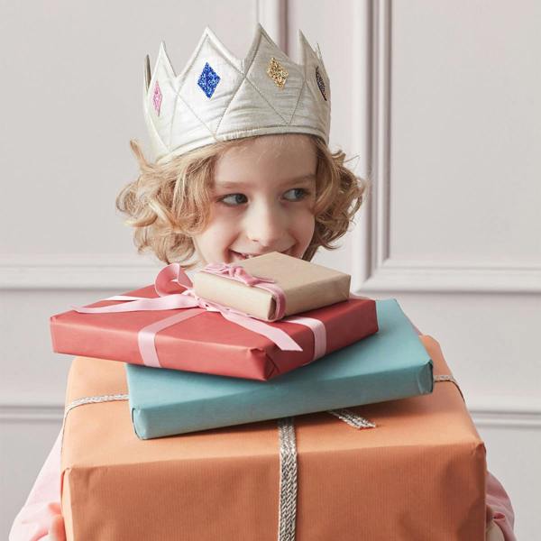 A child wearing a quilted gold lamé fabric crown with sparkling glitter details while holding a large stack of wrapped colourful birthday presents.