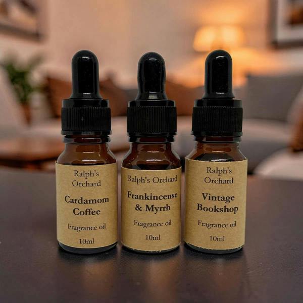 Three bottles of Ralph's Orchard fragrance oils on a wooden surface with a blurred indoor background.