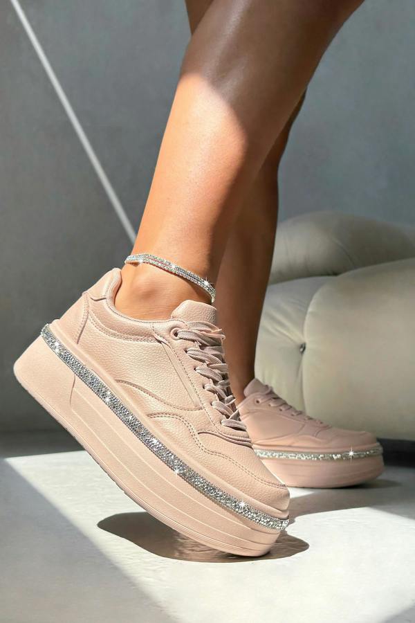 Pink sneakers with glittery details worn by a person on a neutral background