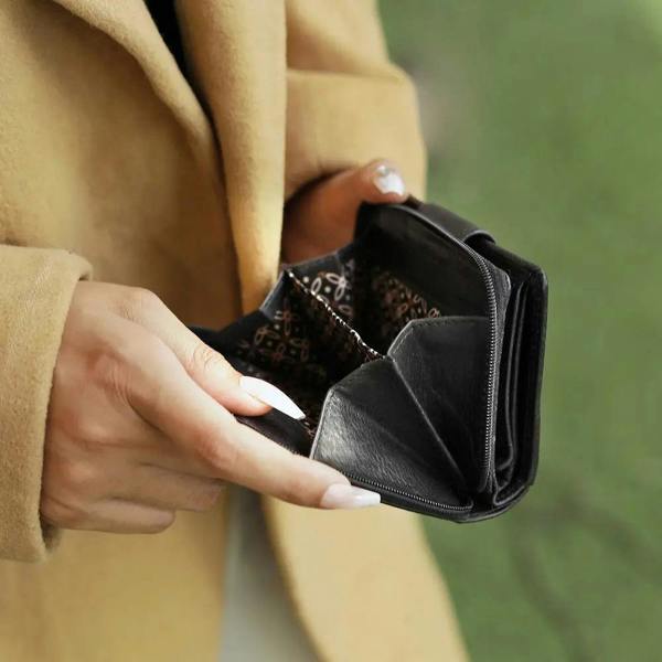 Person holding a black wallet with a blurred green background