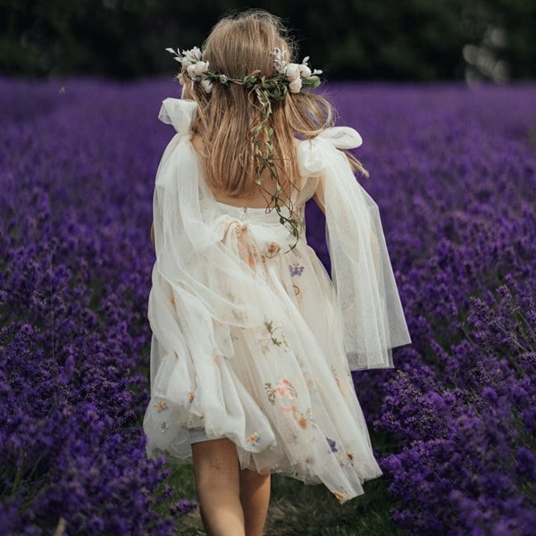 girl in a white dress with floral decorations standing in a lavender field