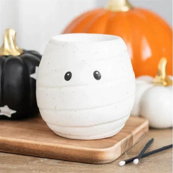 White ceramic mummy-shaped oil burner with black dot eyes and wide top opening