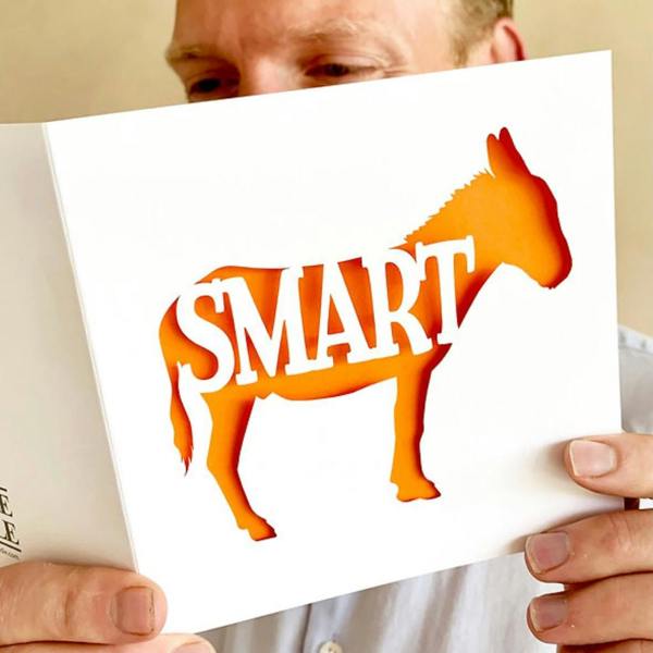 Person holding a white Smart Ass papercut congratulations card with an orange paper insert