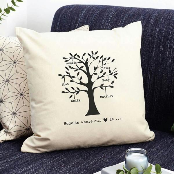 A cream scatter cushion cover from Abode Home & Gifts printed with a black family tree design featuring six names and a heart icon, sitting on a dark blue sofa.