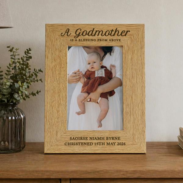 Personalised engraved oak veneer photo frame holding a portrait baby photo, styled on a wooden tabletop next to a vase.