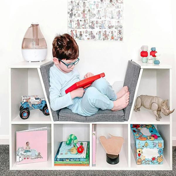 White cube storage shelf with gray cushioned seat, kid playing with toys in cubbies