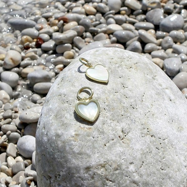 Gold vermeil heart charm hoops displayed on a rock on a beach.