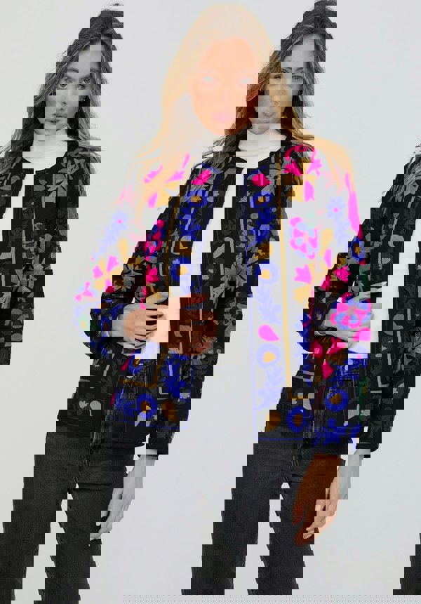 Woman wearing a colorful embroidered jacket on a plain background