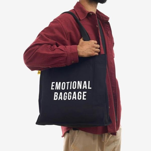 Man over-the-shoulder wearing a dark red jacket carrying the black Emotional Baggage organic cotton tote bag.