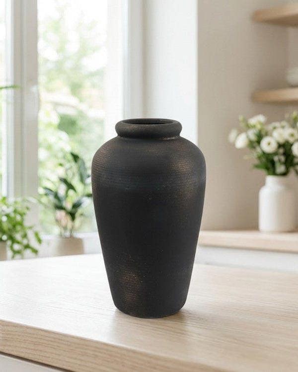 Black vase on a wooden surface with a blurred indoor background