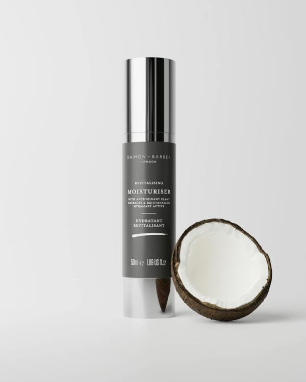 Skincare bottle labeled 'Revitalising Moisturiser' next to a split coconut on a light gray background
