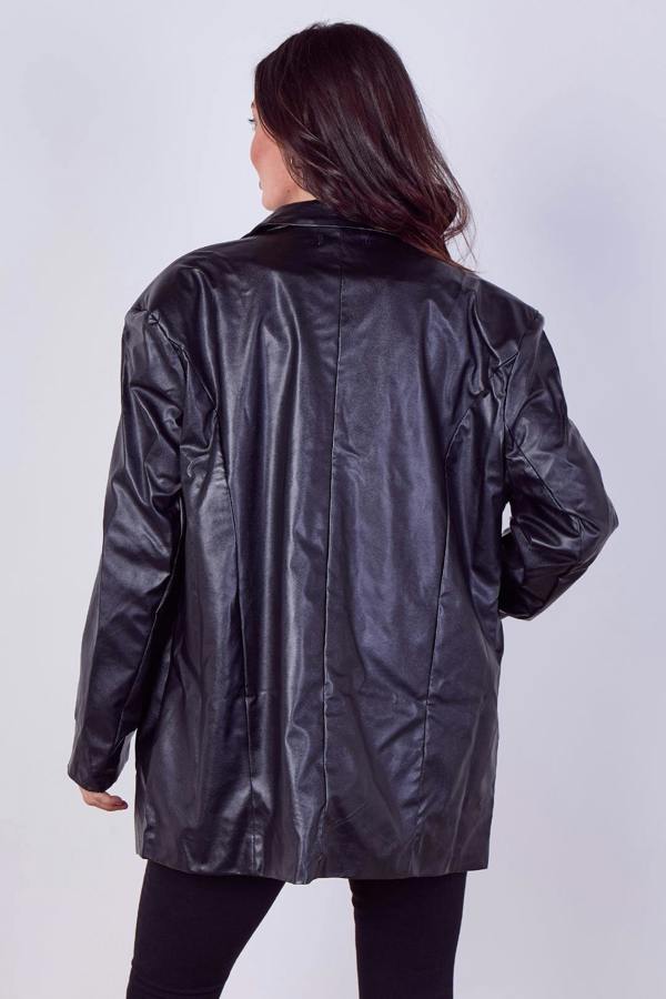 A woman viewed from behind wearing an oversized black faux-leather jacket with a smooth, slightly glossy finish, paired with black pants, against a light gray studio background.