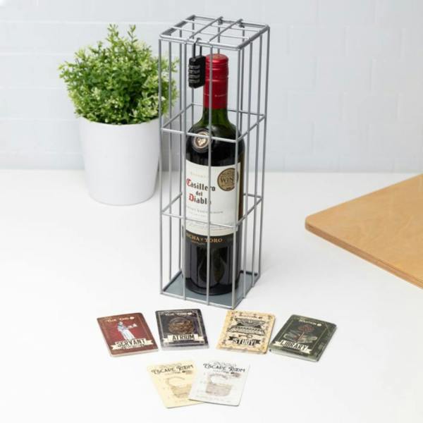 A bottle of red wine locked inside a silver metal wire cage with a black combination lock, surrounded by escape room themed clue cards on a white countertop.