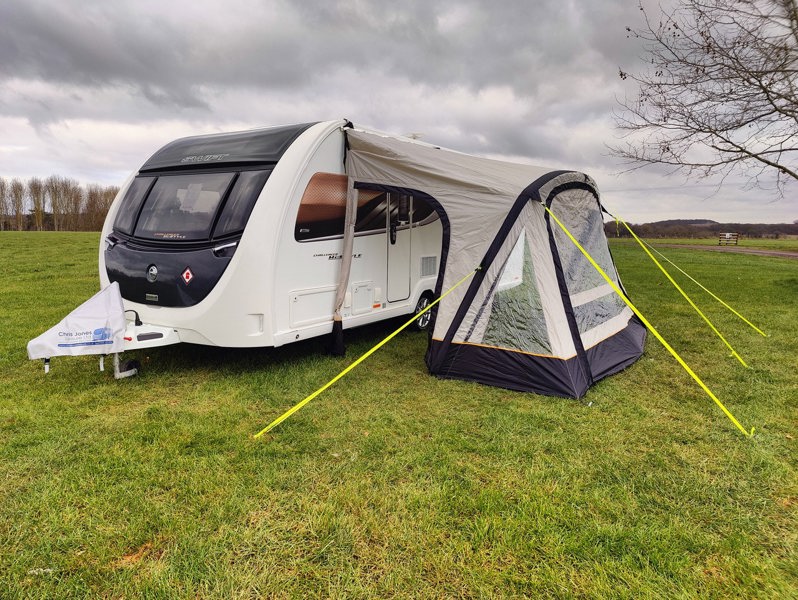 The OLPRO View Lite Breeze 390 Caravan Awning pictured in a Caravan site attached to a caravan with the side doors open.