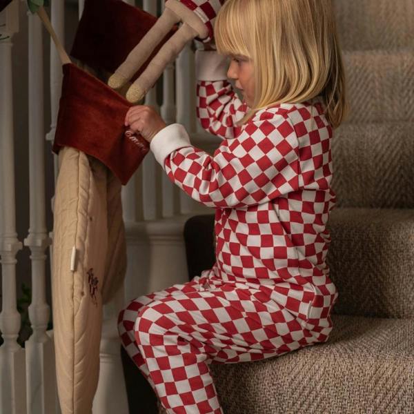 A young blonde child wearing red and white checkerboard Christmas pyjamas, sitting on carpeted stairs while looking into a personalised velvet holiday stocking.