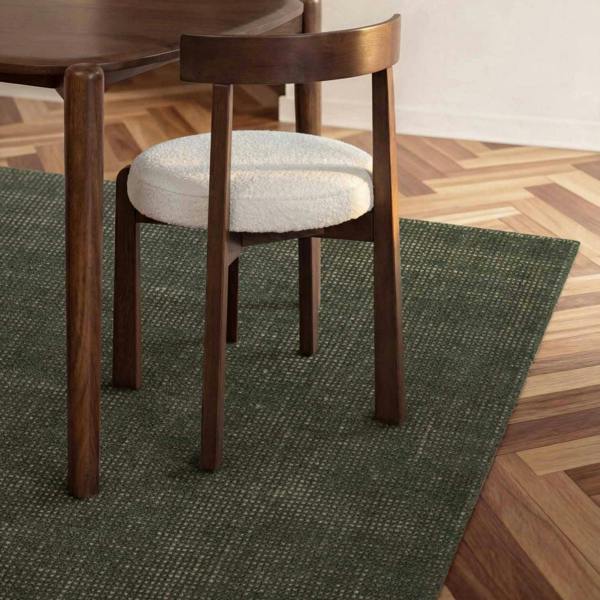Wooden chair with a white cushion on a green rug in a room with wooden flooring.