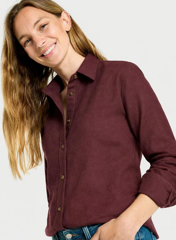 A woman wearing a long-sleeve button-up shirt in a deep burgundy color, paired with blue jeans, against a plain light gray background.