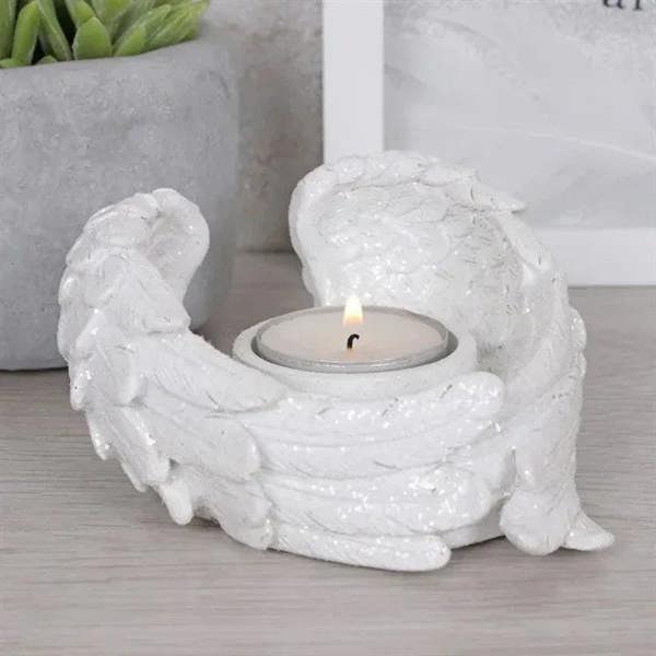 White glitter angel wing candle holder on tabletop with lit tealight in bowl