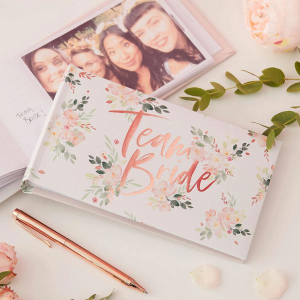 Rose gold foiled Team Bride floral hen party photo album lying flat beside a rose gold pen and green foliage.