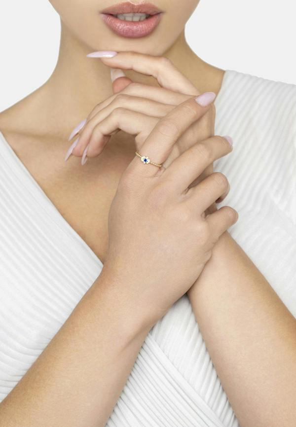Close-up of a woman's hand wearing a ring with a small blue gemstone on a white background