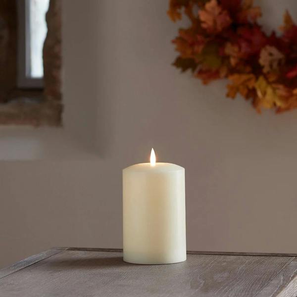 Ivory LED chapel candle on a rustic wooden table with an autumn leaf wreath.