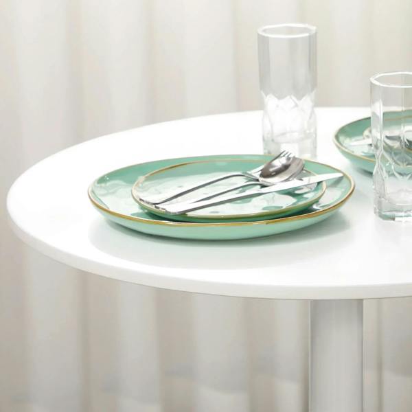 White round pedestal dining table with green-rim plates on top and central column