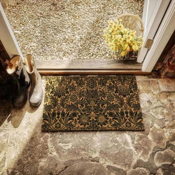 Decorative doormat with floral pattern on stone floor, shoes, and basket of flowers.
