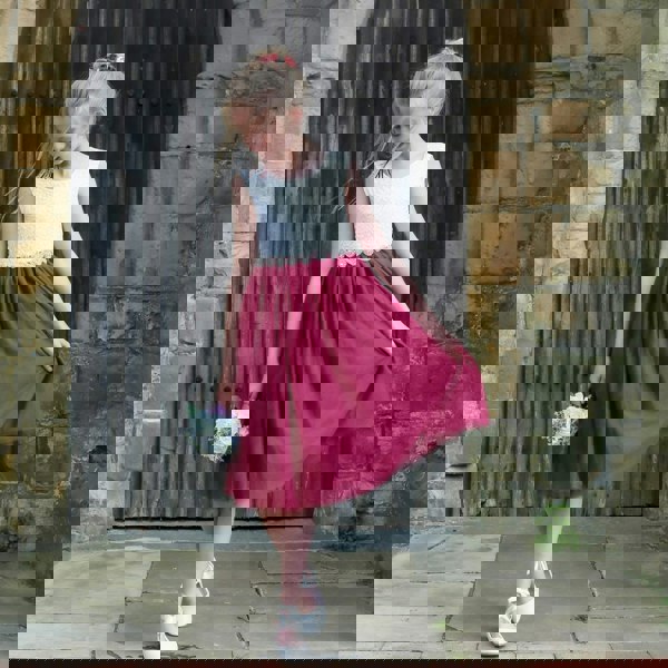 Young girl in a white top and red skirt standing in front of a stone wall.