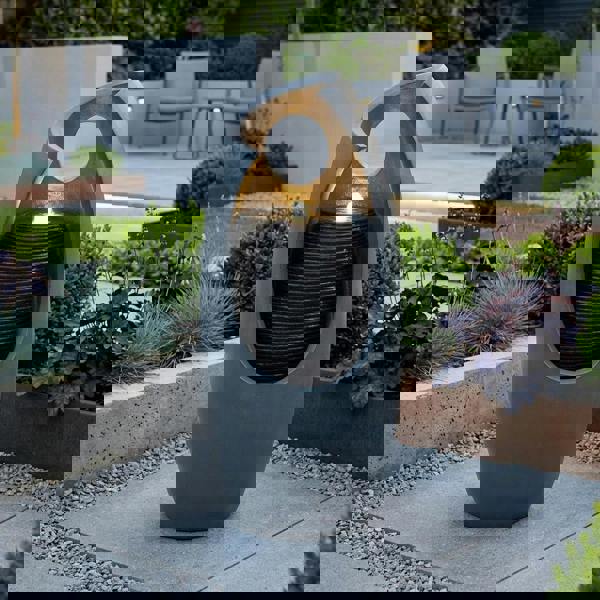 Sleek gray electric water feature with a modern design, featuring cascading water and a soft glowing light, surrounded by lush greenery