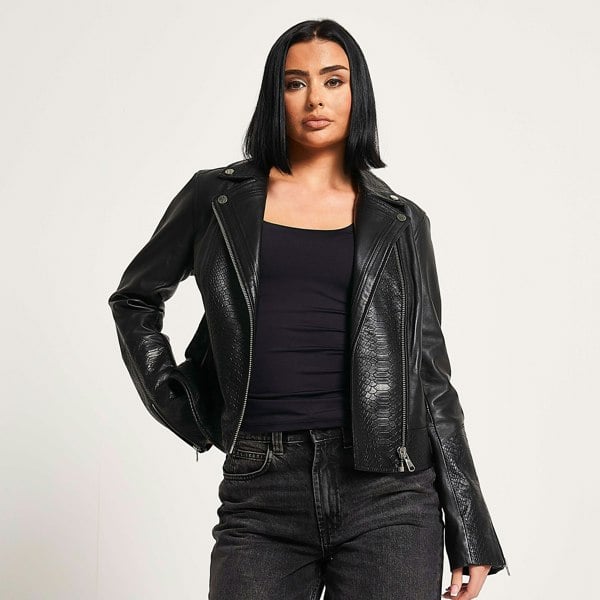 Image shows a woman wearing a black leather biker jacket and all black outfit. The leather jacket has an embossed snake print pattern.