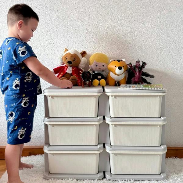 Cream kids storage unit with six drawers, child standing beside and reaching for contents.