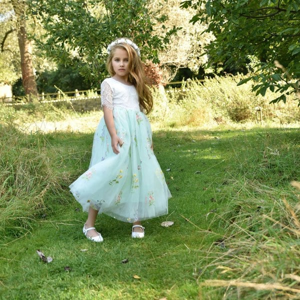 Young girl in a light green dress standing in a grassy field with trees in the background