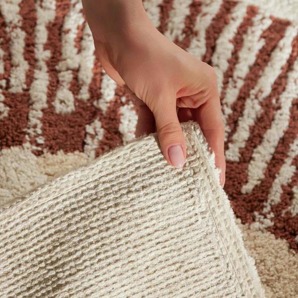 Hand touching a textured beige fabric against a patterned brown and beige background