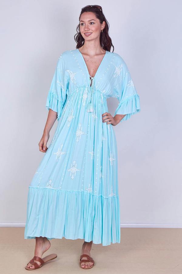 Woman wearing a light blue dress with white patterns against a plain background