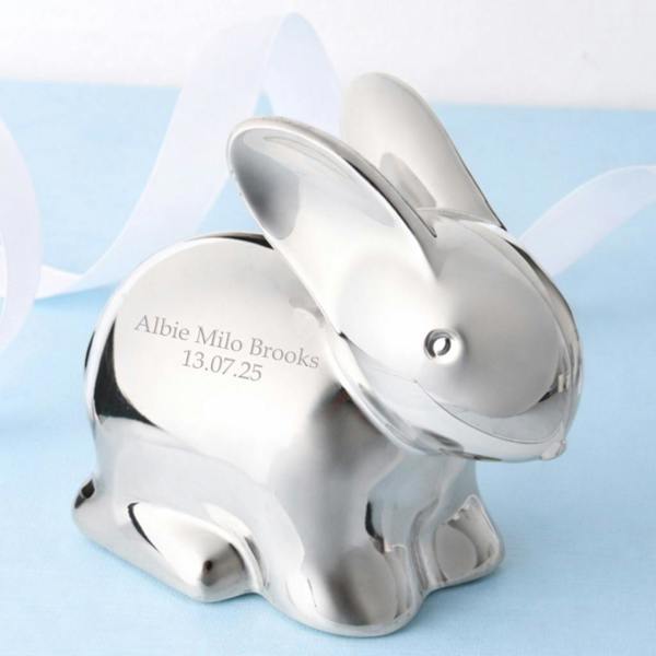 A personalised silver-plated rabbit money box with a custom engraved name and date, set against a light blue background with a white ribbon.