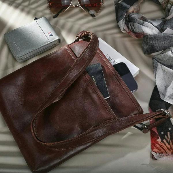Cognac leather bag with sunglasses, wallet, and phone on a light surface