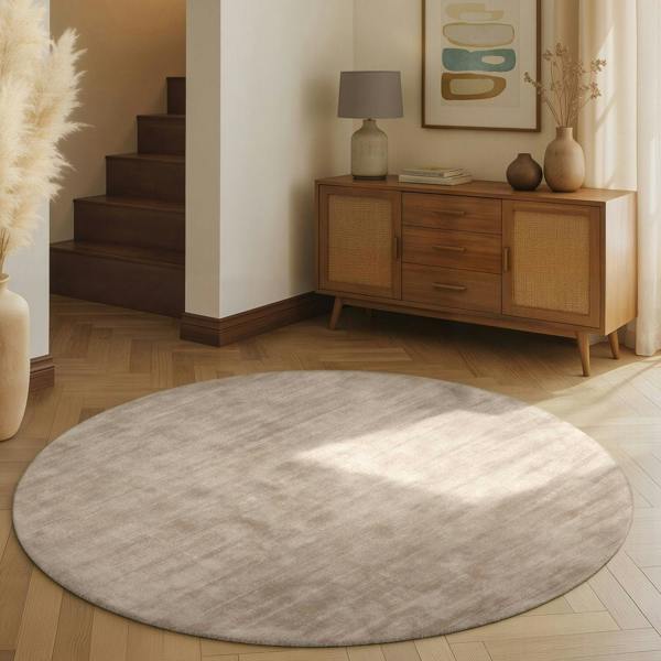 Round gray rug on a wooden floor with a wooden cabinet and decorative items in the background.